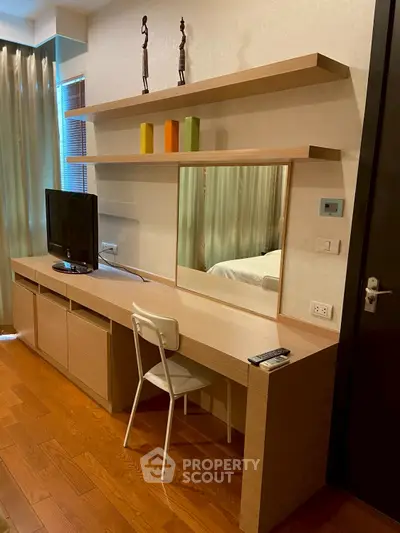 Modern bedroom with sleek wooden desk, TV, and decorative shelves in a stylish apartment.