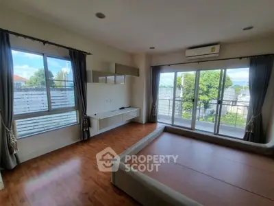 Spacious bedroom with large windows and balcony access, featuring wooden flooring and modern design.