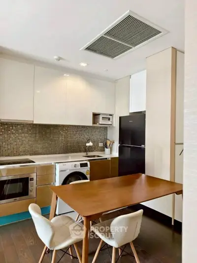 Modern kitchen with sleek appliances and dining area, featuring a washing machine and stylish decor.