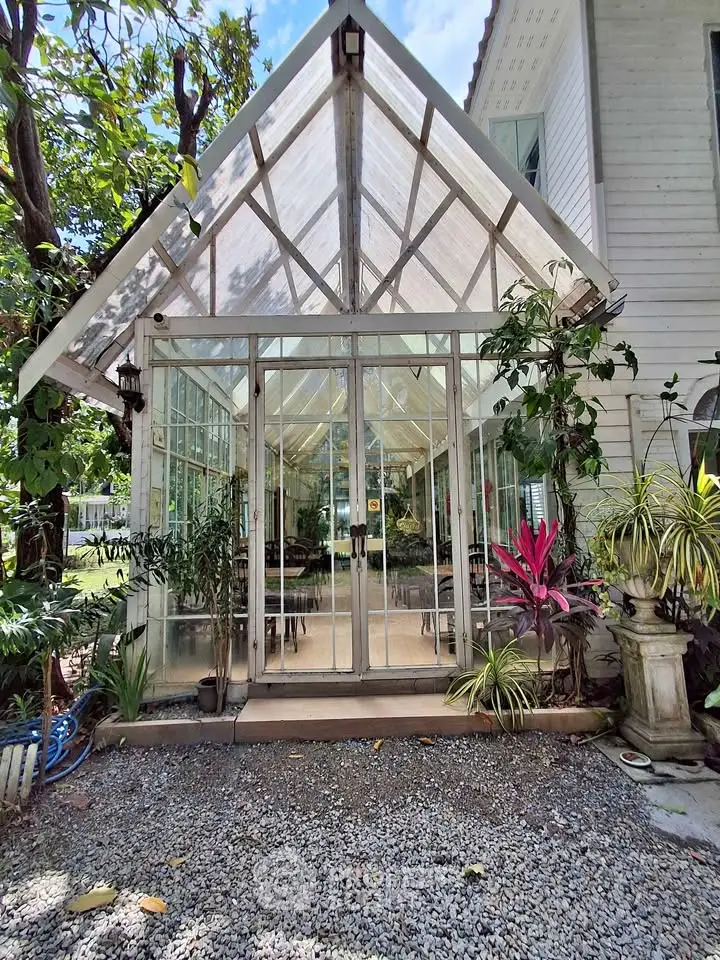 Charming glass conservatory entrance with lush greenery and gravel path