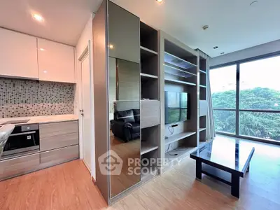 Modern living room with open kitchen and large windows offering lush green views.