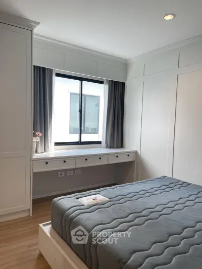 Cozy bedroom with modern design, featuring a large window and built-in storage, perfect for urban living.