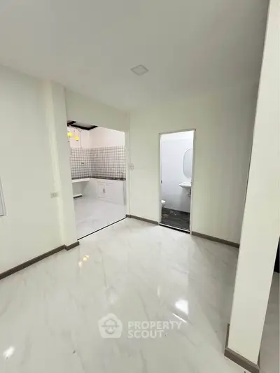 Spacious open-plan living area with modern kitchen and sleek white tiles, perfect for contemporary living.