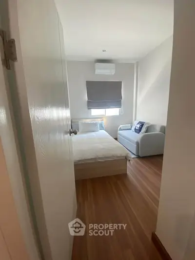 Cozy bedroom with wooden flooring, featuring a bed and a small sofa, perfect for relaxation.