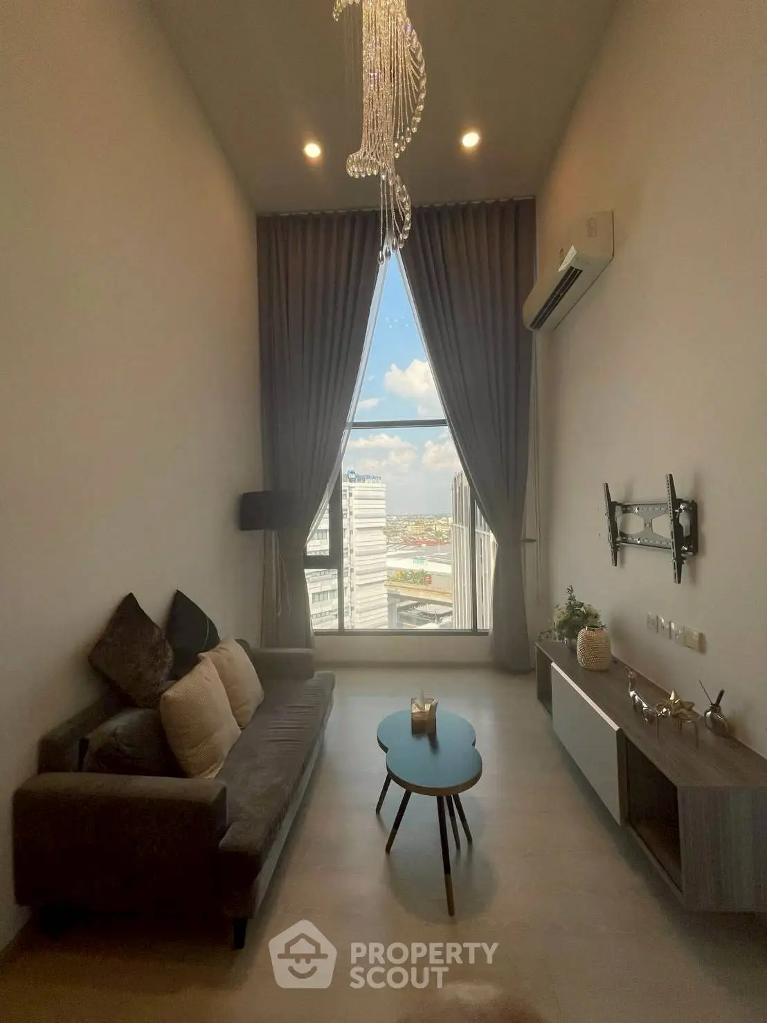 Modern living room with high ceiling and large window offering city view, featuring elegant decor and cozy seating.