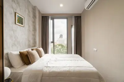 Modern bedroom with large window offering city view, featuring cozy bed and stylish decor.