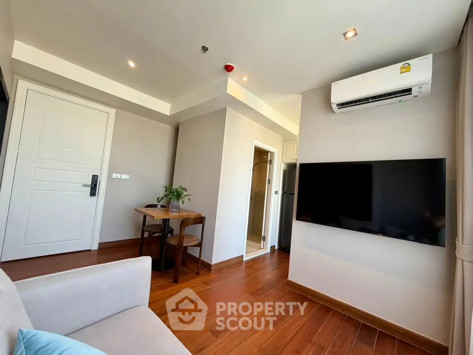 Modern living room with wooden flooring, wall-mounted TV, and air conditioning in a cozy apartment.