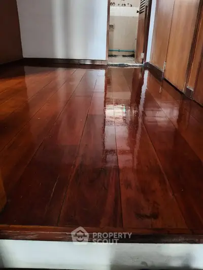 Polished wooden floor in a residential hallway leading to a bathroom.