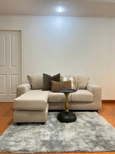 Cozy living room with plush beige sofa and modern side table on a soft rug.