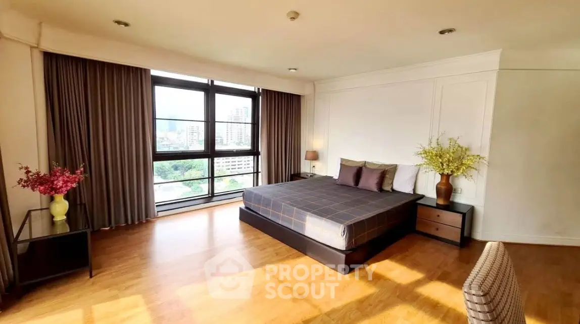 Spacious bedroom with large windows and city view, featuring elegant decor and ample natural light.