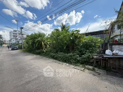 Vacant land plot in urban area with lush greenery and clear blue sky, ideal for development opportunities.