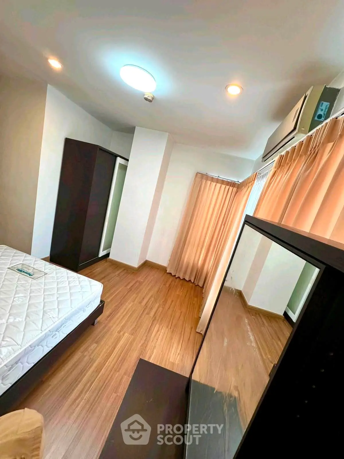 Spacious bedroom with wooden flooring, large wardrobe, and natural light from window.