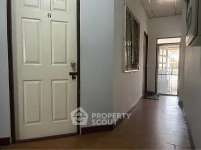 Spacious corridor with wooden flooring and secure door, ideal for residential or office use.