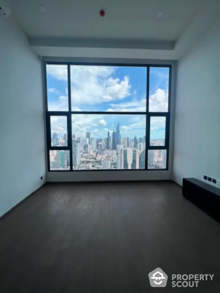 Spacious room with stunning city view through large windows in modern high-rise building.