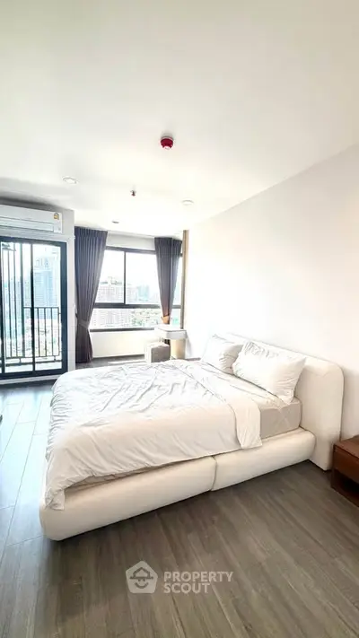 Spacious bedroom with modern decor and city view, featuring a cozy bed and large windows for natural light.
