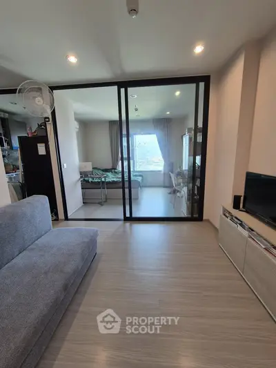Modern living room with sliding glass doors leading to a cozy bedroom, featuring sleek furniture and natural light.