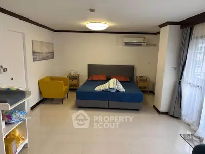 Spacious bedroom with modern decor and natural light, featuring a cozy seating area and air conditioning.