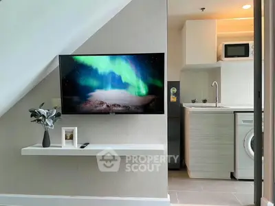 Modern apartment interior with TV, washing machine, and compact kitchen area.