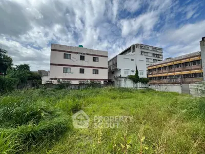 Spacious urban plot with lush greenery and adjacent buildings, perfect for development opportunities.