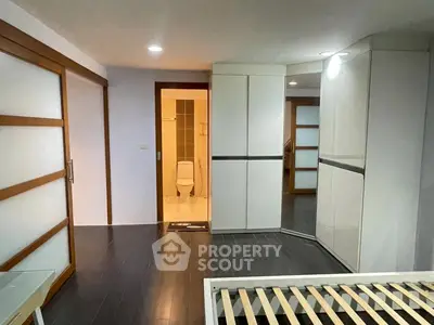 Modern bedroom with sleek design and adjacent bathroom, featuring wooden flooring and ample storage.