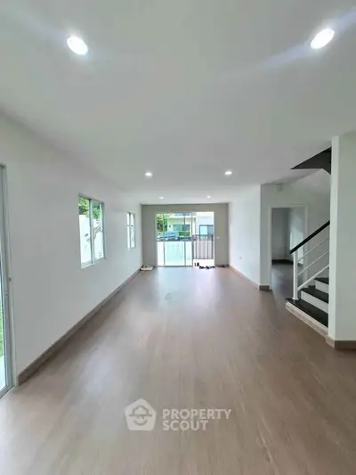 Spacious open-plan living room with wooden flooring and large windows for natural light.