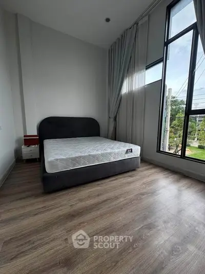 Spacious bedroom with large windows and modern decor, offering a serene view and ample natural light.