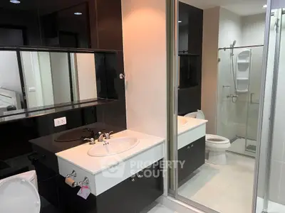Modern bathroom with sleek black and white design, featuring a glass shower and large mirror.