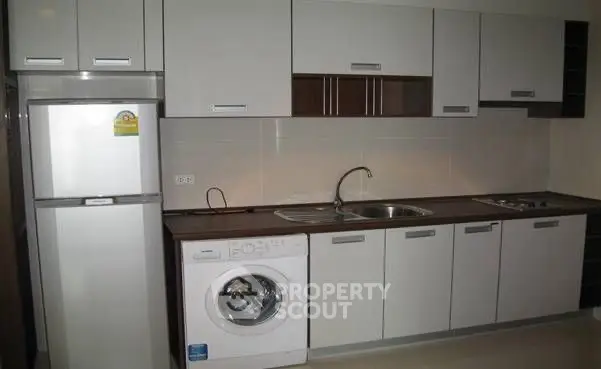 Modern kitchen with sleek cabinets, washing machine, and compact fridge.