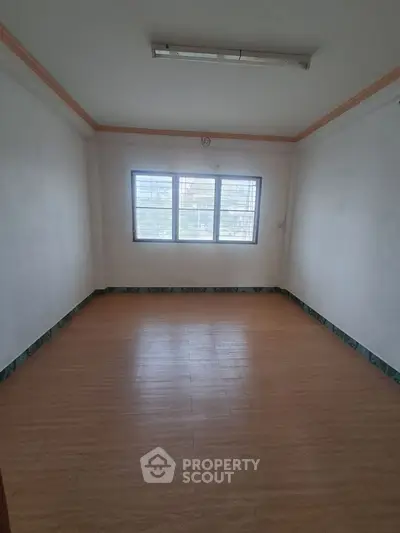 Spacious empty room with large window and wooden flooring, ideal for customization.