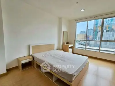 Spacious bedroom with large window offering city views, featuring modern furniture and natural light.