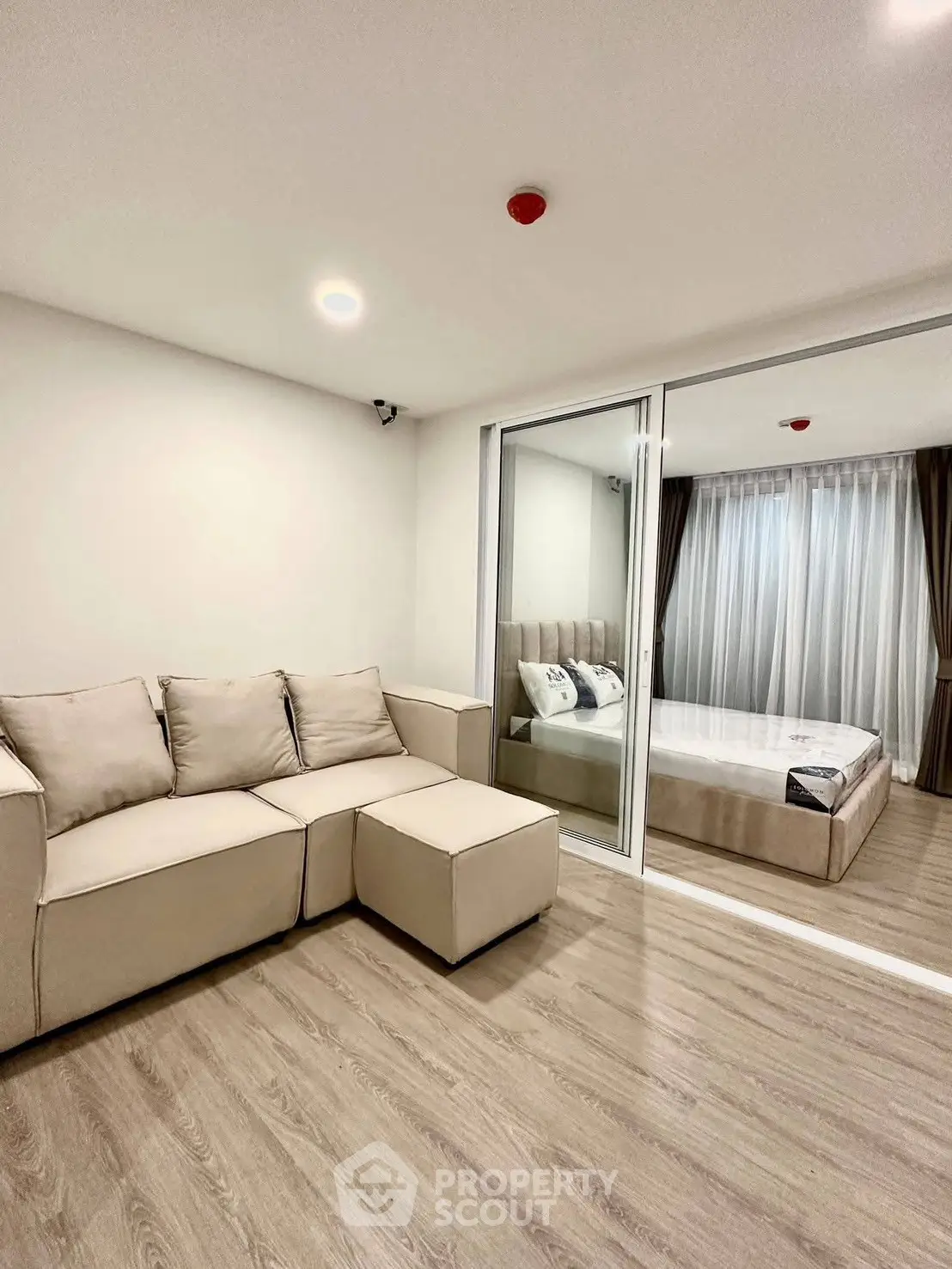 Modern apartment interior with cozy living room and elegant bedroom separated by glass doors.