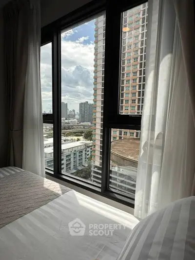 Cozy bedroom with large window offering stunning cityscape views in a modern high-rise building.