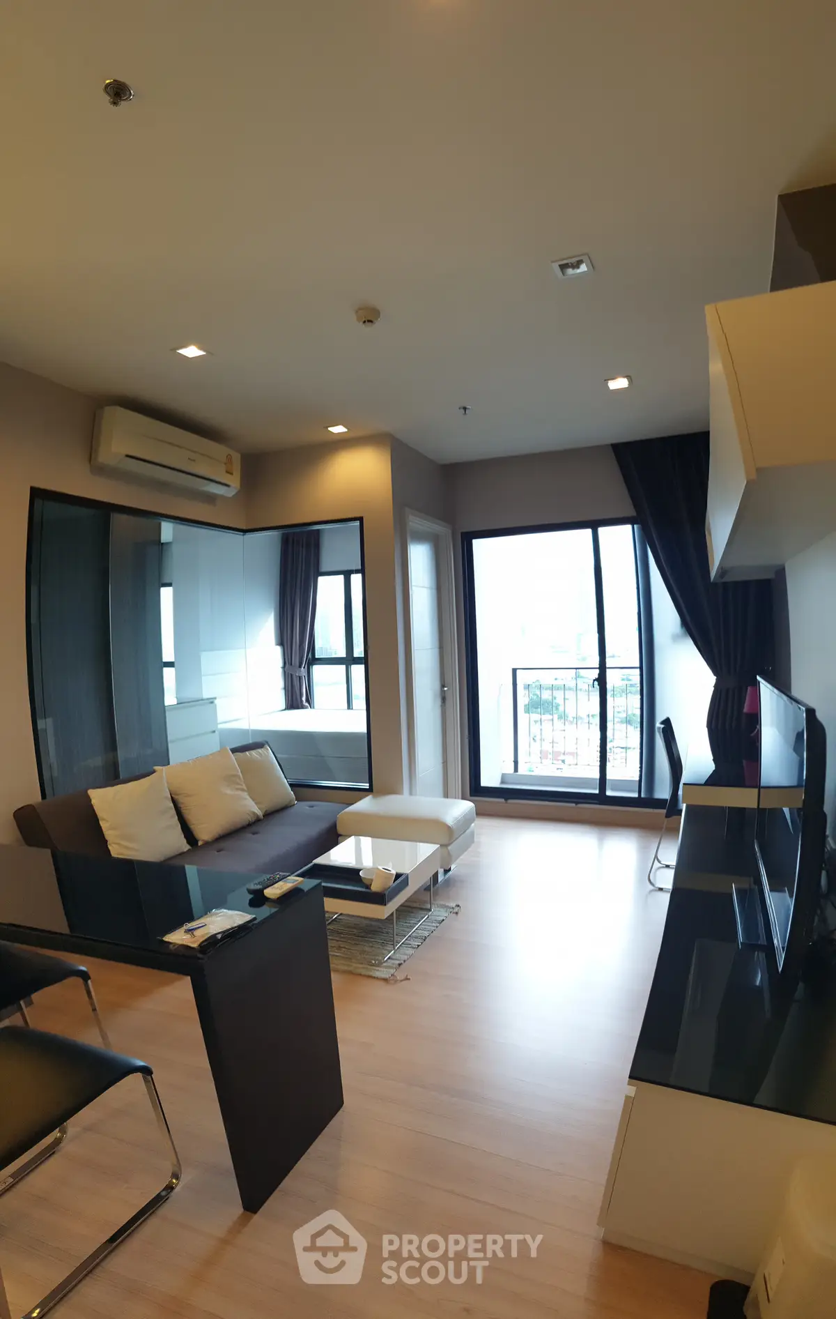Modern living room with sleek furniture and large windows offering natural light and a balcony view.