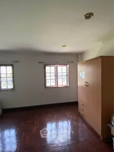 Spacious bedroom with wooden flooring and ample natural light from large windows.