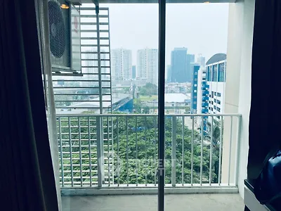 Modern apartment balcony with city skyline view and lush greenery.