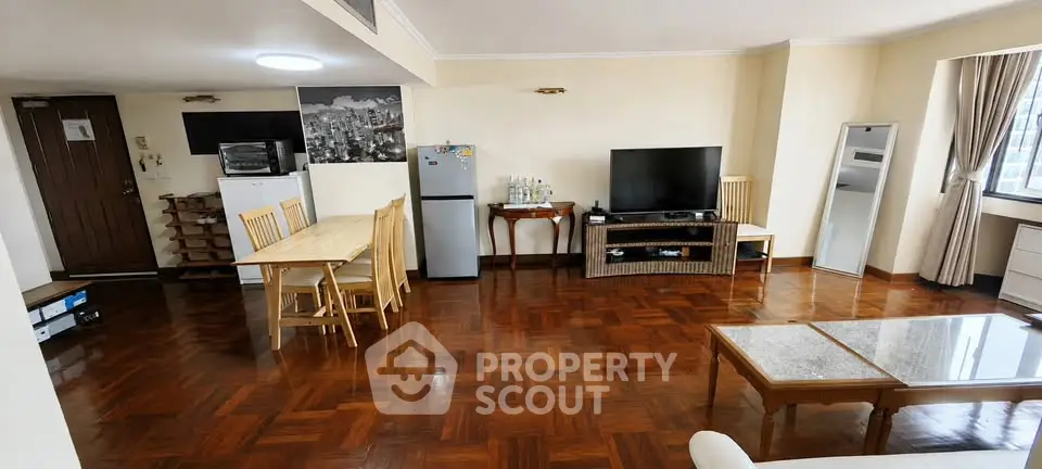 Spacious living room with wooden flooring, dining area, and modern appliances in a cozy apartment.