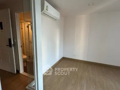 Spacious empty room with wooden flooring and air conditioning, adjacent to a modern bathroom.
