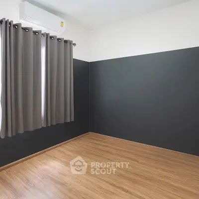 Minimalist empty room with wooden flooring and dark accent wall, perfect for customization.