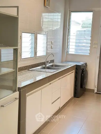 Modern kitchen with sleek cabinetry and washing machine, featuring ample natural light and tiled flooring.