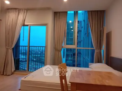 Modern bedroom with large windows and city view, featuring a wooden table and bed.