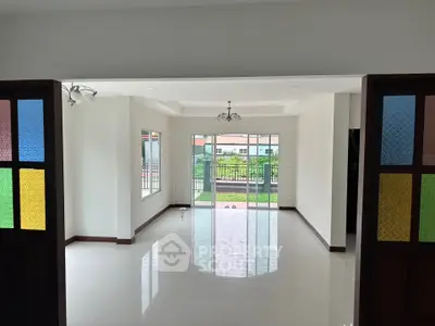 Spacious living room with colorful glass doors and garden view, perfect for family gatherings.