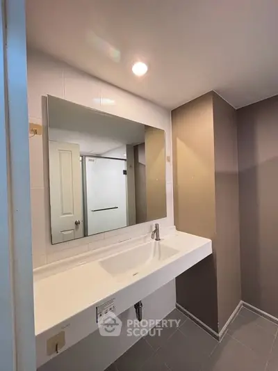 Modern bathroom with sleek design and large mirror, featuring a spacious sink and neutral color palette.