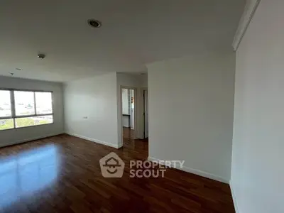 Spacious empty room with wooden flooring and large window offering natural light.