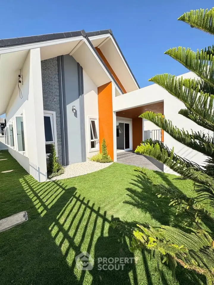 Modern architectural home exterior with lush green lawn and striking orange accents.