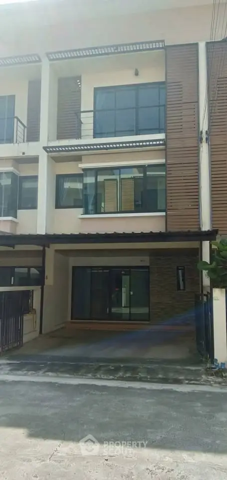 Modern three-story townhouse with large windows and balcony in a quiet neighborhood.