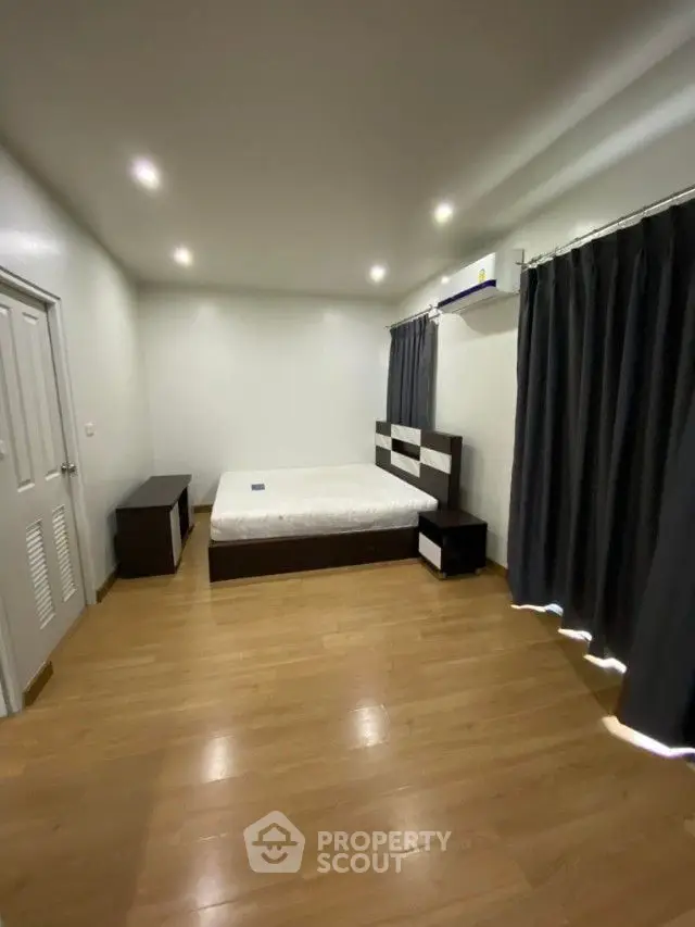 Spacious bedroom with polished wooden flooring, modern recessed lighting, and elegant dark curtains, offering a serene and comfortable living space.