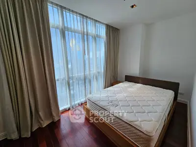 Spacious bedroom with large window and hardwood floors in modern apartment.