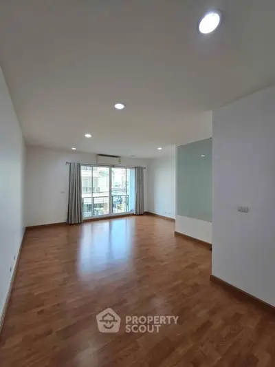 Spacious empty living room with wooden flooring and large window, perfect for customization.