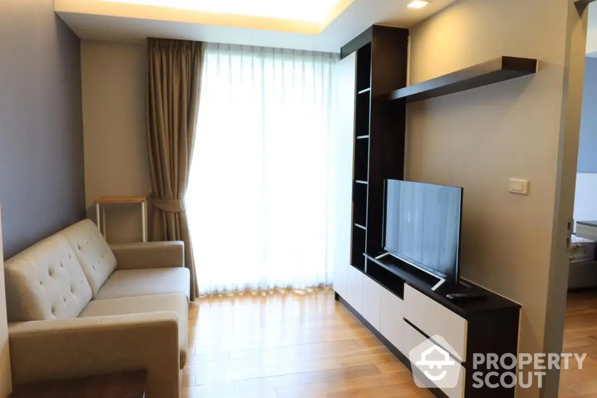 Modern living room with cozy sofa and sleek TV unit, featuring natural light from large window.