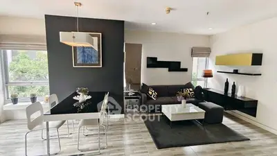 Modern living room with stylish decor and dining area, featuring sleek furniture and large windows.